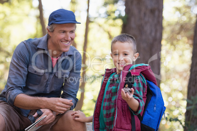 Happy man looking at boy holding pine cone in forest