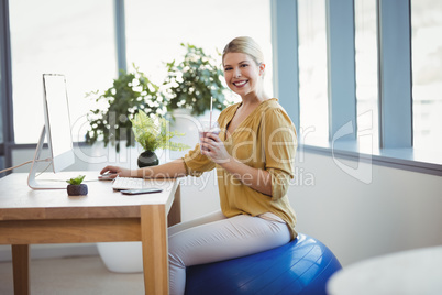 Portrait of smiling executive sitting on fitness ball while working at desk