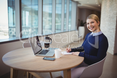 Smiling female executive writing on notepad in office