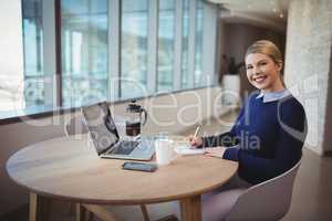 Smiling female executive writing on notepad in office