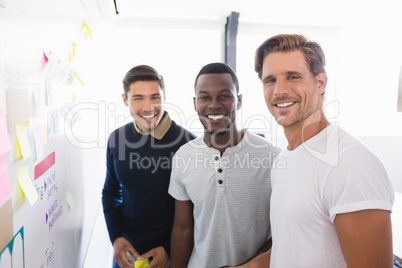 Portrait of smiling businessmen standing by whiteboard