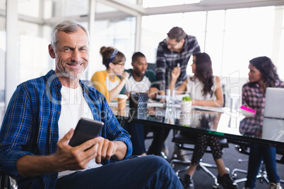 Portrait of happy businessman using mobile phone with team working in background