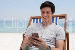 Man sitting on sunlounger and using mobile phone on the beach