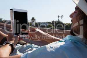 Man relaxing on hammock and using digital tablet on the beach