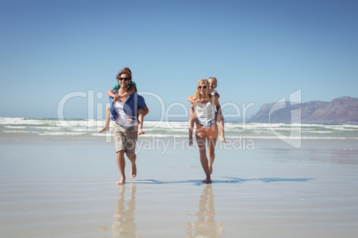 Happy parents piggybacking their children on shore at beach