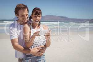 Cheerful couple using mobile phone at beach