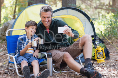 Happy father and son taking selfie while having hot drink in forest