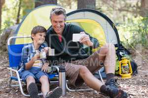 Happy father and son taking selfie while having hot drink in forest