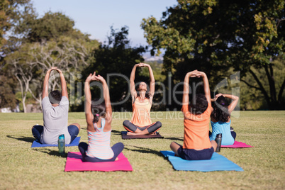 Trainer teaching children stretching while sitting on mat