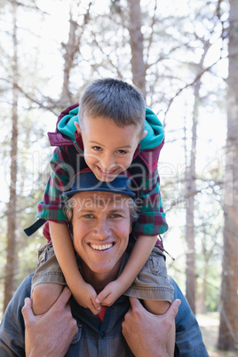 Happy boy sitting on shoulders of father in forest