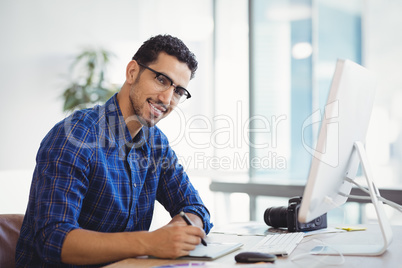 Portrait of smiling graphic designer using graphic tablet at desk