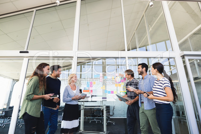 Smiling business colleagues standing against glass wall