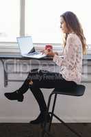 Businesswoman holding coffee cup while working on laptop