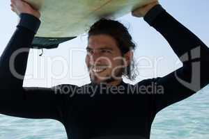 Surfer in wetsuit carrying surfboard over head at beach coast