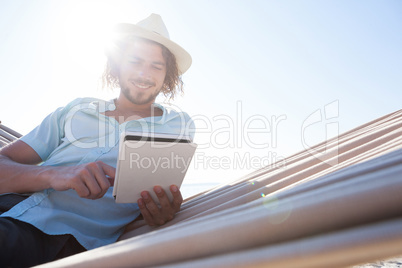 Man relaxing on hammock and using digital tablet on the beach