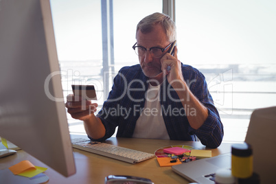 Businessman talking on mobile phone while holding credit card at office