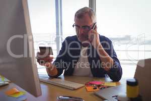 Businessman talking on mobile phone while holding credit card at office