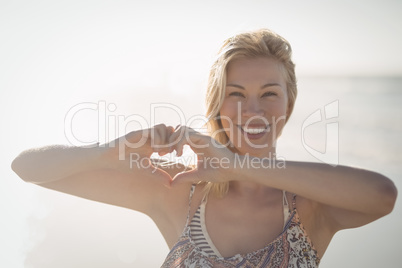 Portrait of woman making heart shape with hands at beach