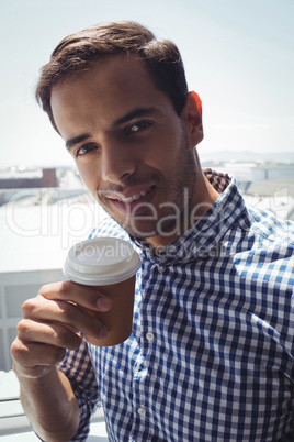 Thoughtful young businessman holding coffee cup by window in office