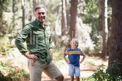 Father and son with hands on hips standing in forest