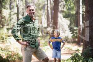 Father and son with hands on hips standing in forest