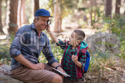 Boy showing magnifying glass to father while hiking in forest