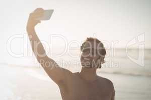 Smiling shirtless man taking selfie at beach