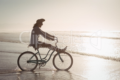 Side view of cheerful woman riding bicycle on shore at beach