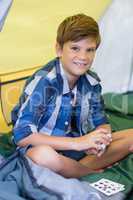 Smiling boy playing cards while sitting in tent