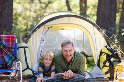 Smiling father and son with digital tablet resting in tent at campsite