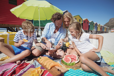 Happy family sitting together by fruits on blanket at beach