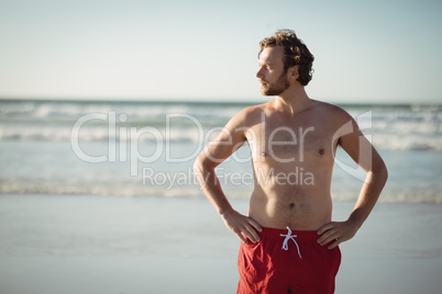 Thoughtful shirtless man standing with hands on hip at beach