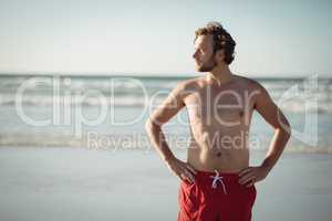 Thoughtful shirtless man standing with hands on hip at beach