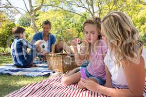 Mother and daughter blowing bubble while father and son playing with football in park