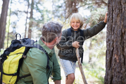 Boy looking at father while standing by tree trunk