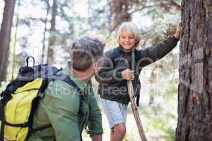 Boy looking at father while standing by tree trunk