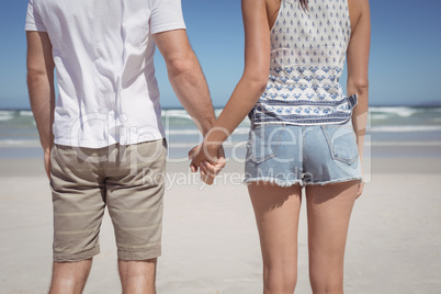 Mid section of young couple holding hands at beach