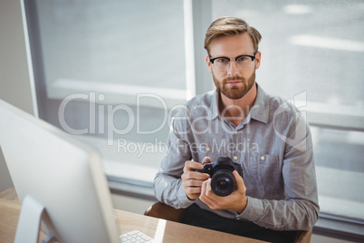 Portrait of confident executive holding digital camera at desk