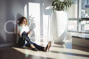 Beautiful executive sitting on floor and using mobile phone