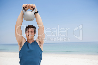 Young man lifting kettlebell at beach