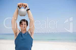 Young man lifting kettlebell at beach