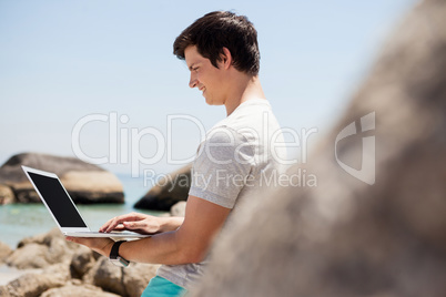 Man leaning on the rocks and using laptop at the sea coast