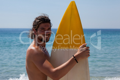 Smiling surfer with surfboard standing at beach coast