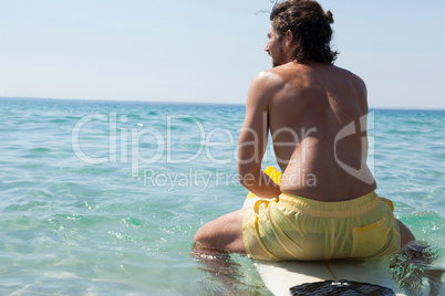 Surfer sitting on surfboard at seacoast
