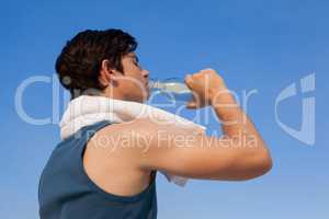 Man drinking water from bottle against blue sky