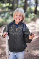 Smiling little boy holding pine cone while standing in forest