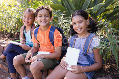 Friends holding books while sitting on retaining wall at natural parkland