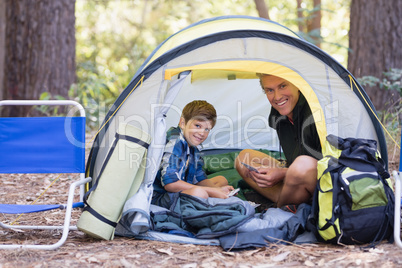 Father and son sitting inside tent while hiking in forest