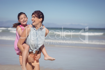 Cheerful mother piggybacking daughter at beach