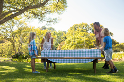 Family spreading the tablecloth on picnic table